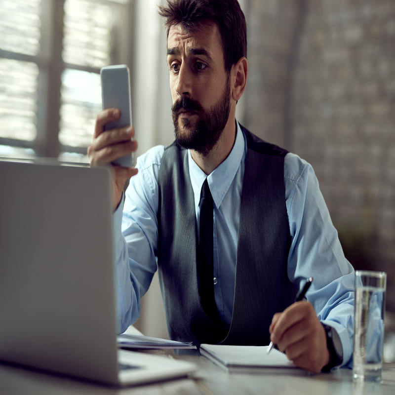 Young businessman reading text message on cell phone while worki